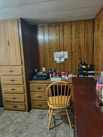 Wood paneling accents, built-in wooden cabinetry, tiled flooring, wood-finish desk with storage, and a drop ceiling