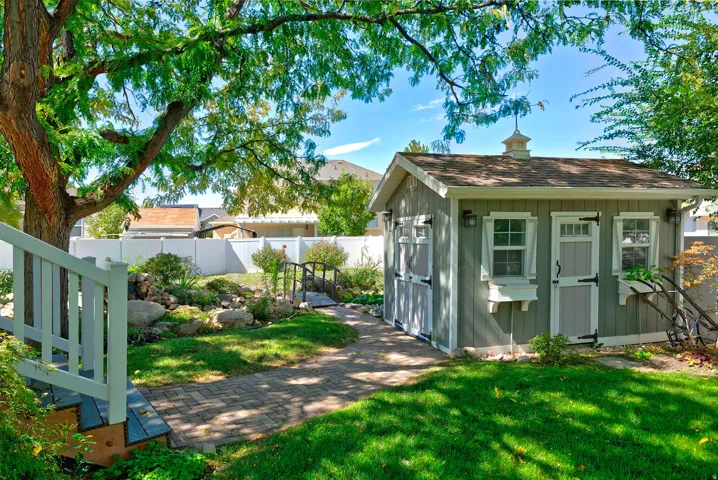 Spacious backyard featuring a storage shed, established tree, paved pathway, and tiered landscaping