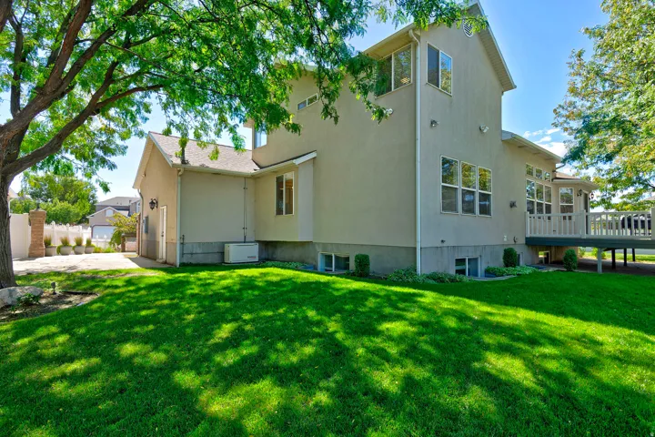 Expansive green lawn with established trees, multi-level stucco exterior, and a spacious elevated deck with white railings