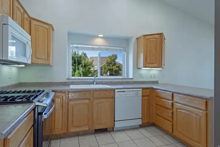 Kitchen featuring wood-finish cabinetry, a built-in microwave, a gas range, a white dishwasher, and a double basin sink