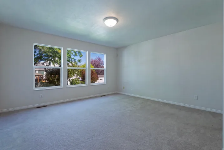 Recessed lighting, three large windows, light gray wall paint, and gray carpet flooring