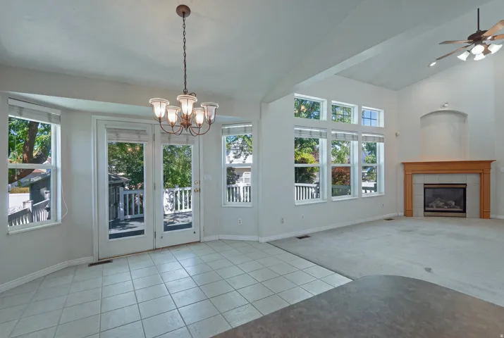 Vaulted ceilings, a gas fireplace with a wood-finish mantel, multiple windows, and a ceiling fan with integrated lighting