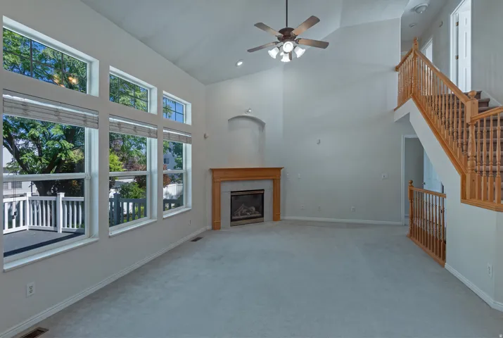 Vaulted ceiling with a ceiling fan, fireplace with a wood-finish mantel, and a multi-pane window array