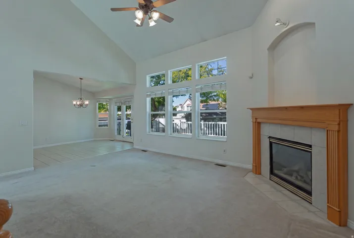 Vaulted ceilings, gas fireplace with tile surround, wood mantel, multiple windows, and a ceiling fan