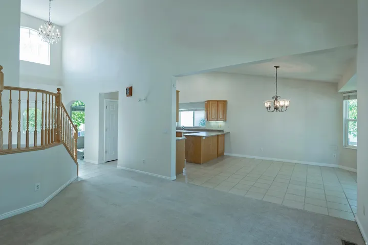 Vaulted ceilings, a crystal chandelier, wood-finish staircase with white balusters, kitchen with wood cabinetry and light countertops, and tile flooring
