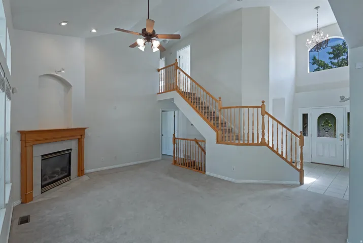 Vaulted ceilings, wood-finish staircase with balusters, tiled fireplace with wooden mantel, recessed lighting, and a crystal chandelier