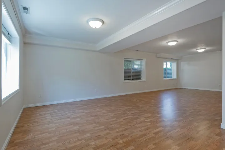 Spacious room featuring wood-finish flooring, multiple windows, crown molding, and flush-mount ceiling lights