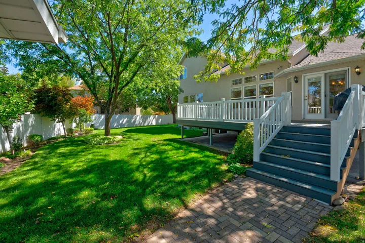 Expansive green lawn with mature trees, white privacy fencing, and a multi-level deck with white railings and steps