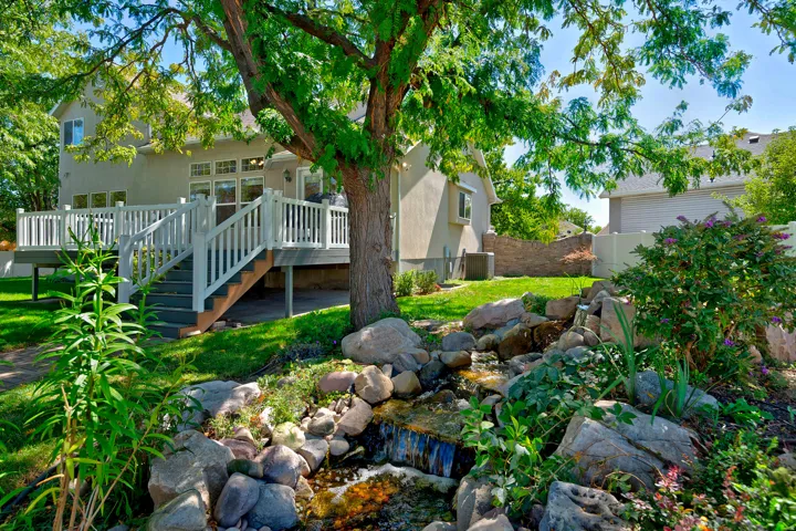 Expansive deck with white railing, stone water feature, mature trees, and a manicured lawn