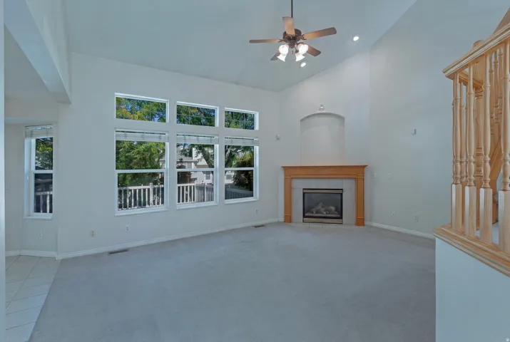 Vaulted ceiling, multiple windows, gas fireplace with wood mantel, ceiling fan with light fixture, and wood balusters