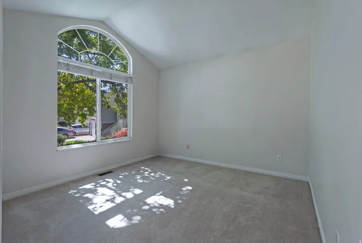 Vaulted ceiling room featuring a large arched window with horizontal blinds and light-toned carpeting
