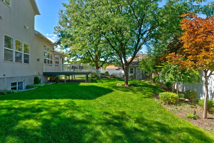 Expansive lawn area with mature trees, raised wood deck, stucco exterior, and a detached shed
