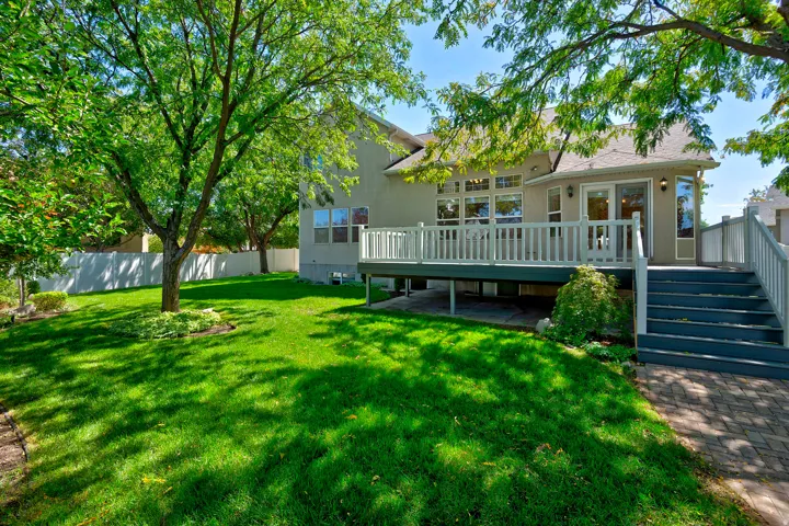 Expansive lawn with mature trees, a multi-level deck, a lower paver patio, and extensive fenestration