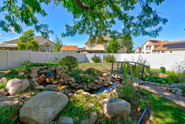 Landscaped backyard featuring a tranquil rock waterfall, a decorative footbridge, and a stone-lined pond