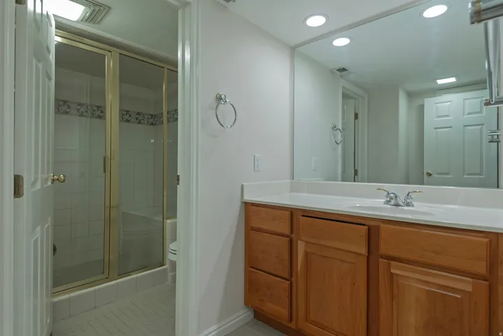 Bathroom featuring a wood-finish vanity with an integrated sink, a large mirror, recessed lighting, and a shower with sliding glass doors