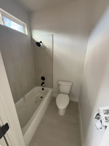 White bathtub with matte black fixtures and light-toned wall tile