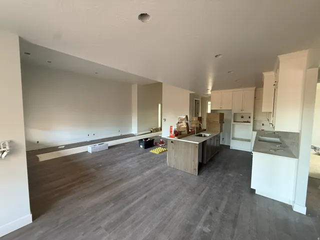 Wood-finish flooring throughout, recessed ceiling lighting, and a kitchen featuring an island with an undermount sink, white upper and lower cabinetry, and stone countertops