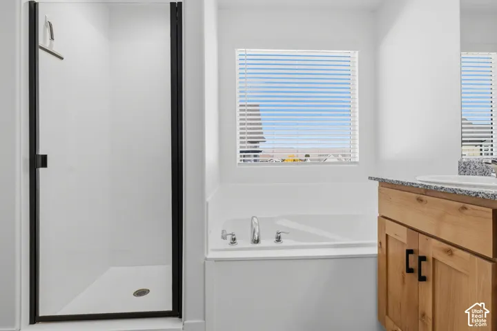 Recessed soaking tub with deck-mounted fixtures, wood-finish vanity with countertop, and a walk-in shower with clear glass enclosure