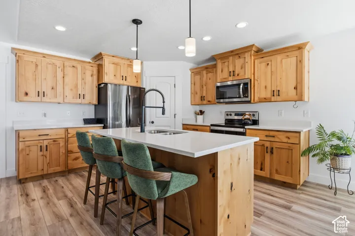 Kitchen featuring light wood cabinetry, stainless steel appliances, a center island with sink, white countertops, and wood-finish flooring