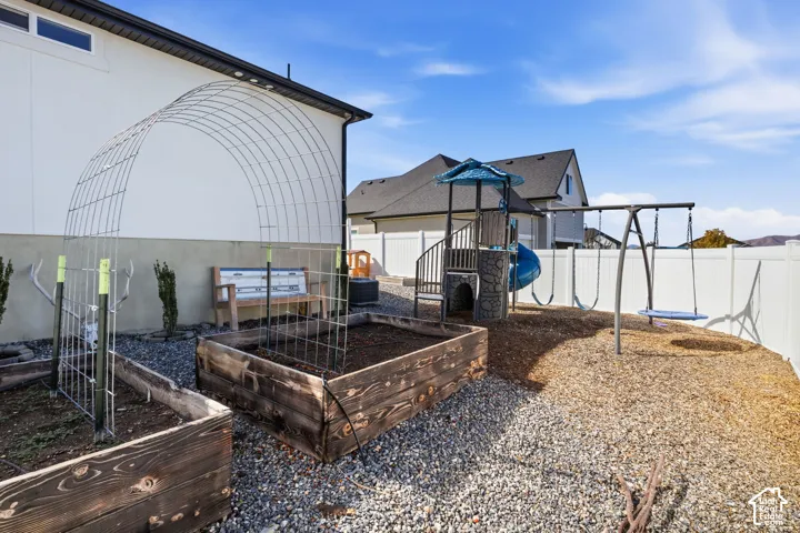 Backyard featuring raised garden beds, a metal arched trellis, and a swing set with a slide