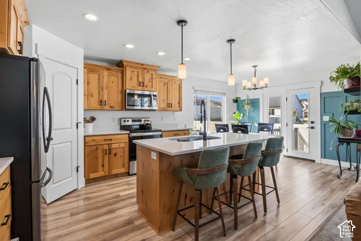Kitchen featuring wood cabinetry, stainless steel appliances, a center island with countertop seating, and wood-finish flooring
