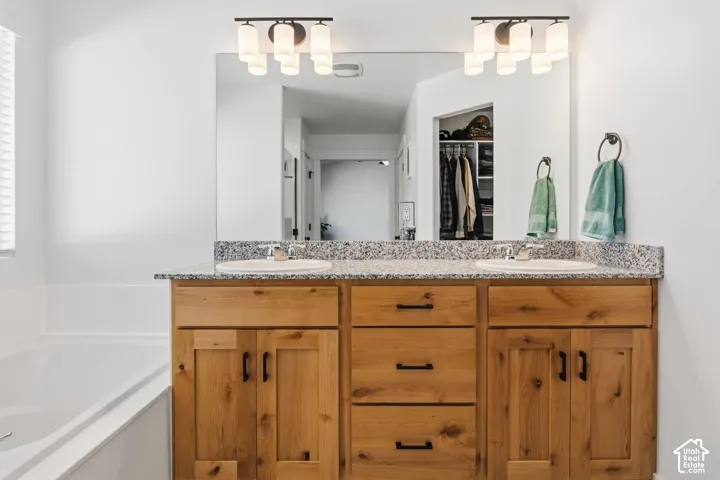 Double vanity with granite countertop and integrated sinks, wood-finish cabinetry, and contemporary lighting fixtures