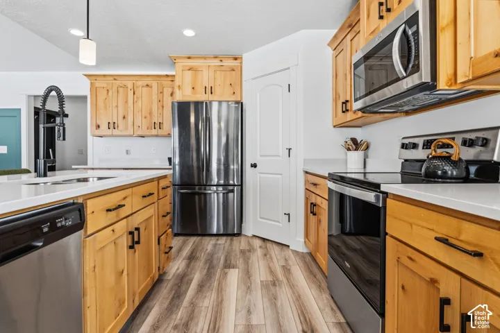 Kitchen featuring wood-finish cabinetry, stainless steel appliances, white countertops, and wood-finish flooring