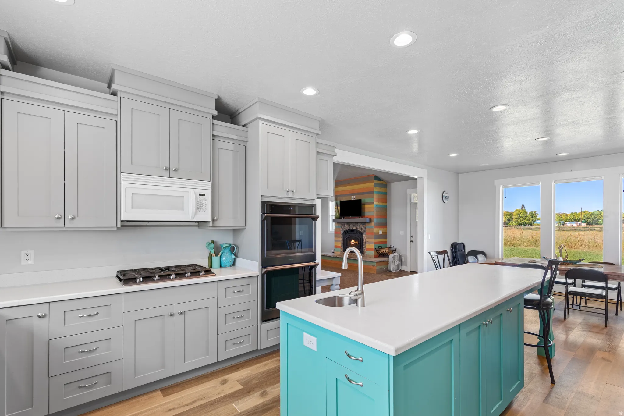 Modern kitchen featuring a turquoise island with sink, stainless steel built-in double oven, built-in microwave, gas cooktop, and wood-finish flooring
