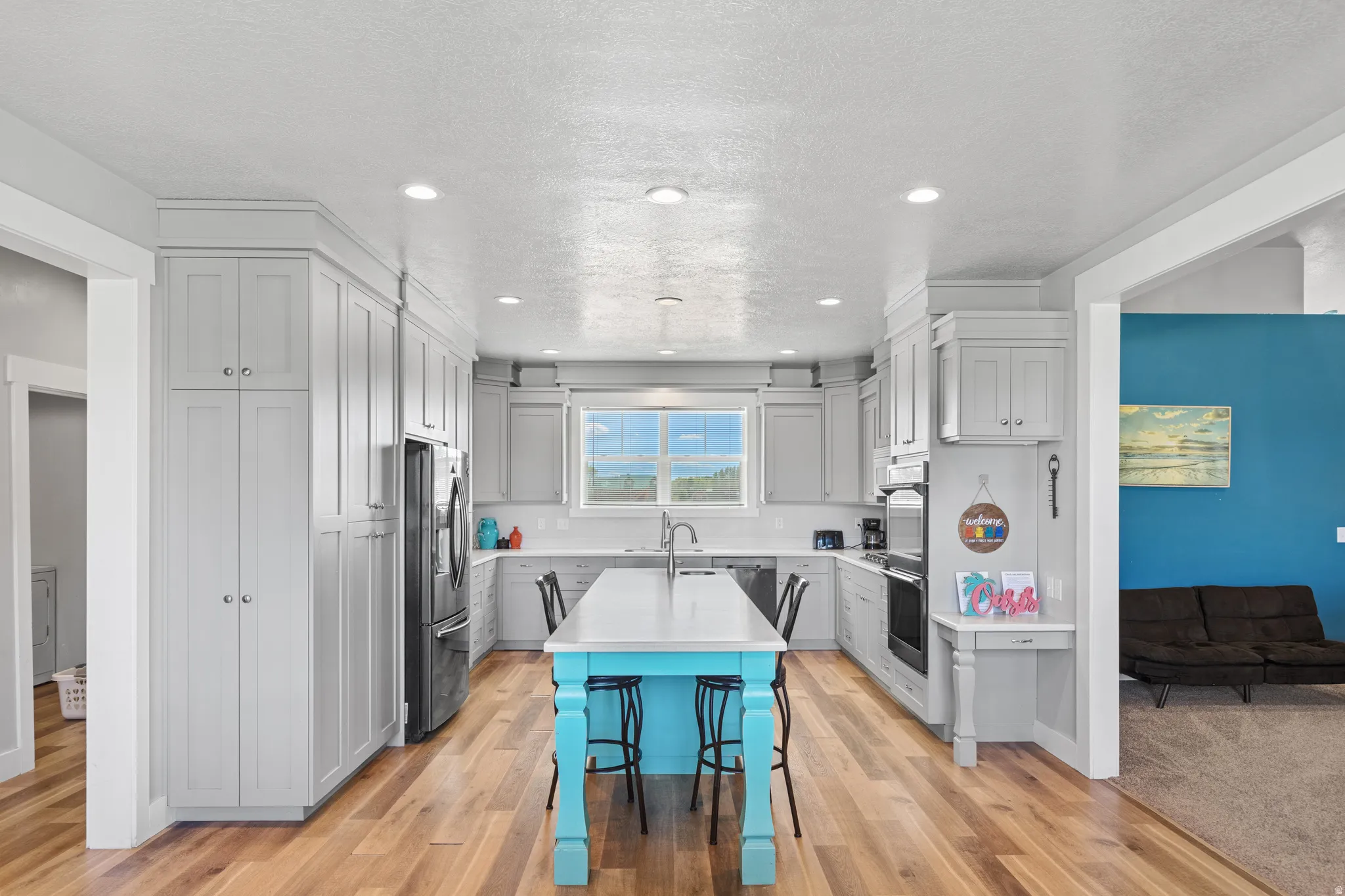 Contemporary kitchen featuring light wood-finish flooring, light-toned cabinetry, stainless steel appliances, and an island with a contrasting base