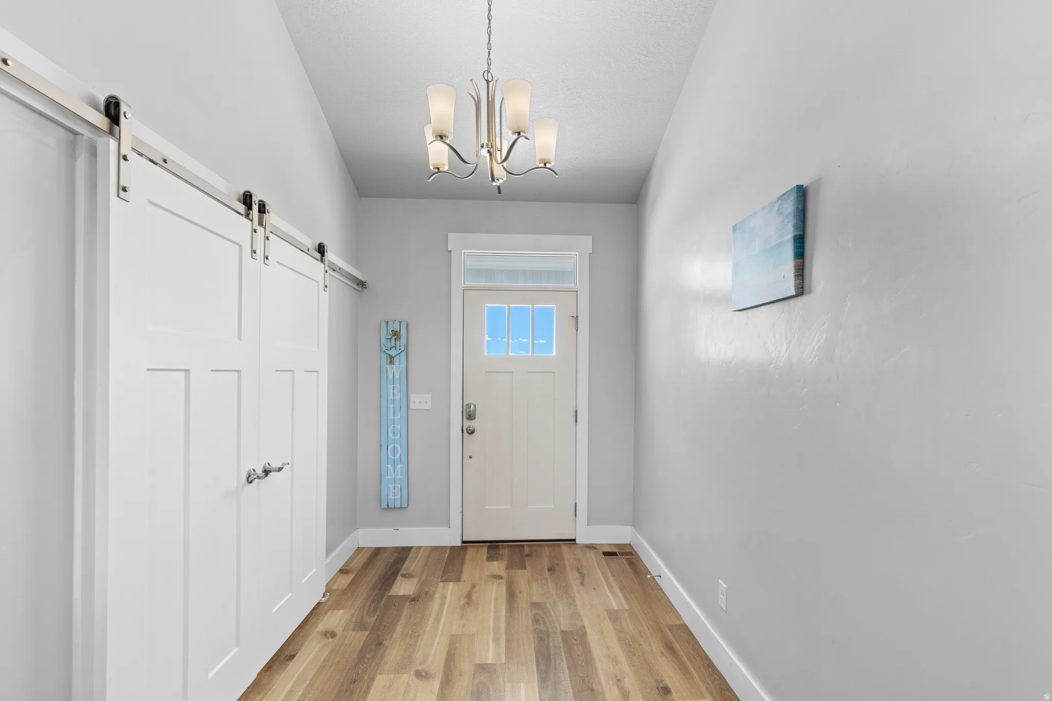 Entryway featuring wood-finish flooring, a contemporary chandelier, a front door with glass panels, and sliding barn doors