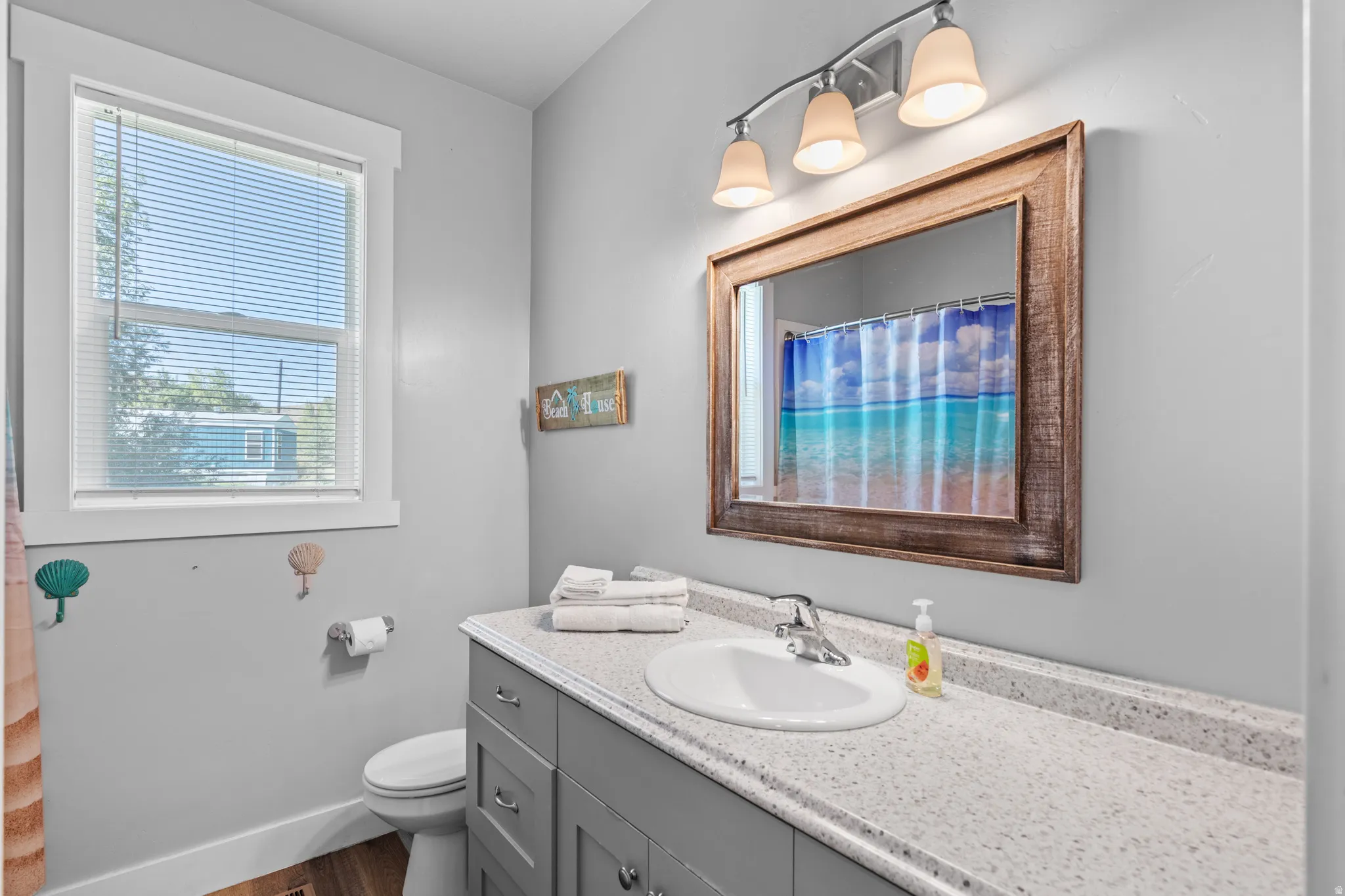 Bathroom featuring a single window, a light gray vanity with a single sink, a light-colored countertop, and a wood-framed mirror
