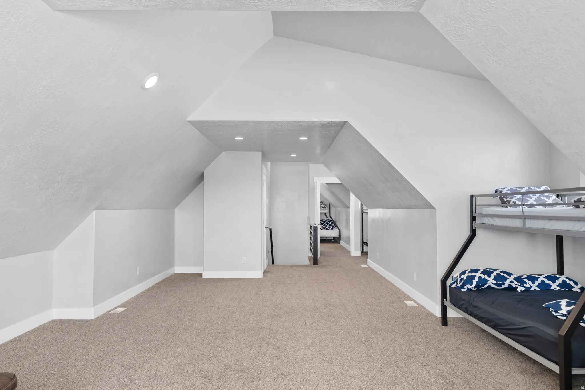 Spacious attic room featuring sloped ceilings, recessed lighting, and neutral carpeting