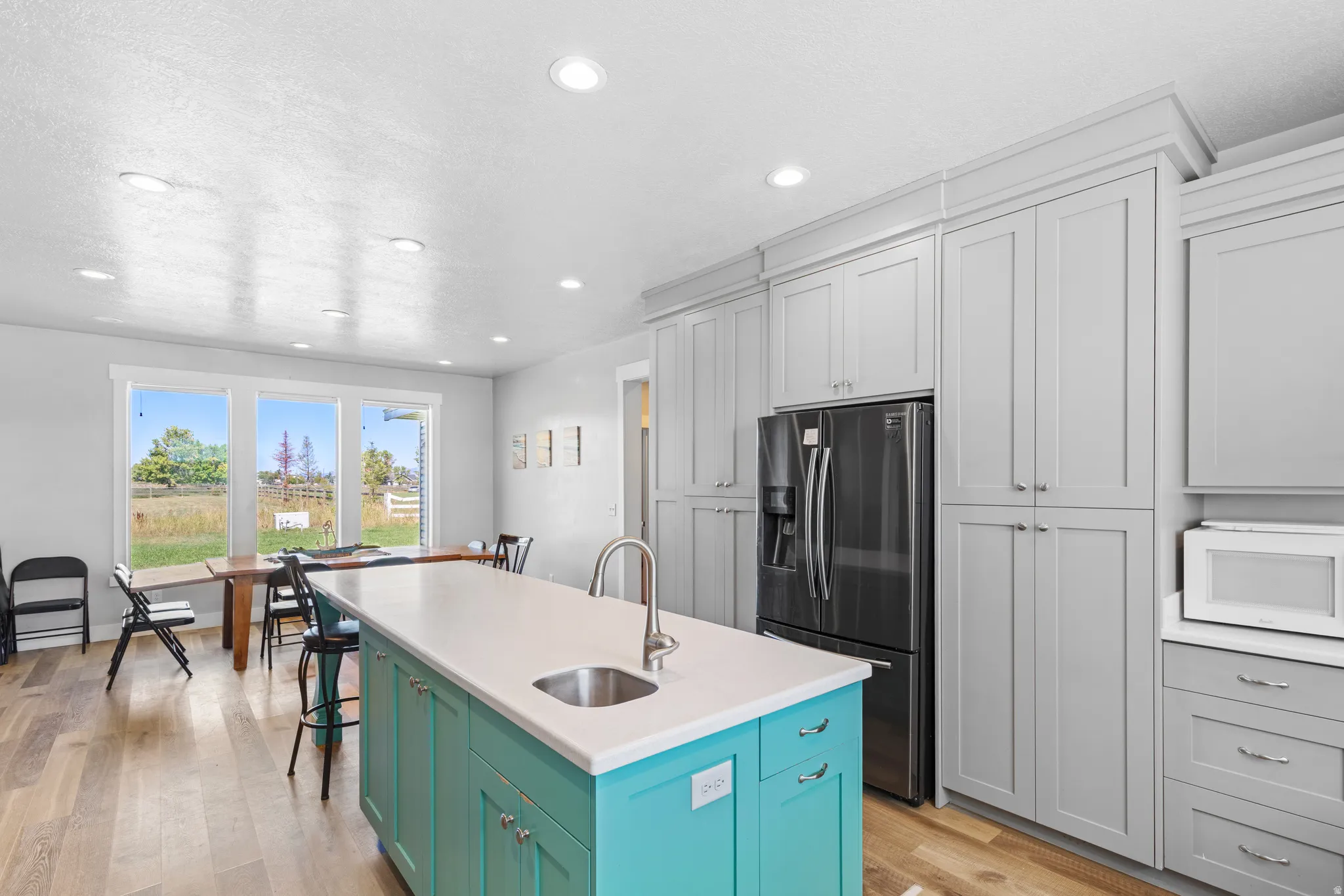 Kitchen featuring a turquoise island with a white countertop, stainless steel sink, wood-finish flooring, and recessed lighting