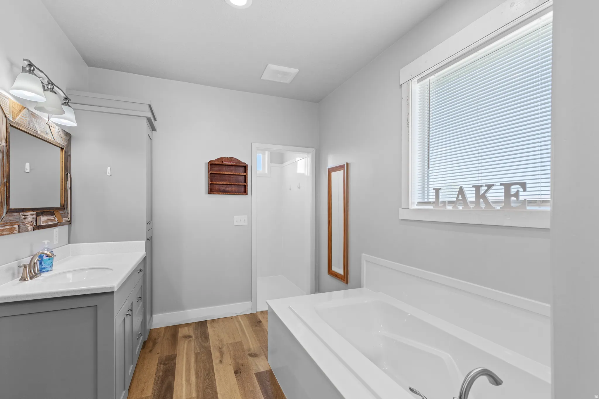 Bathroom featuring a vanity with a white countertop and undermount sink, wood-finish flooring, built-in bathtub, and a window with blinds