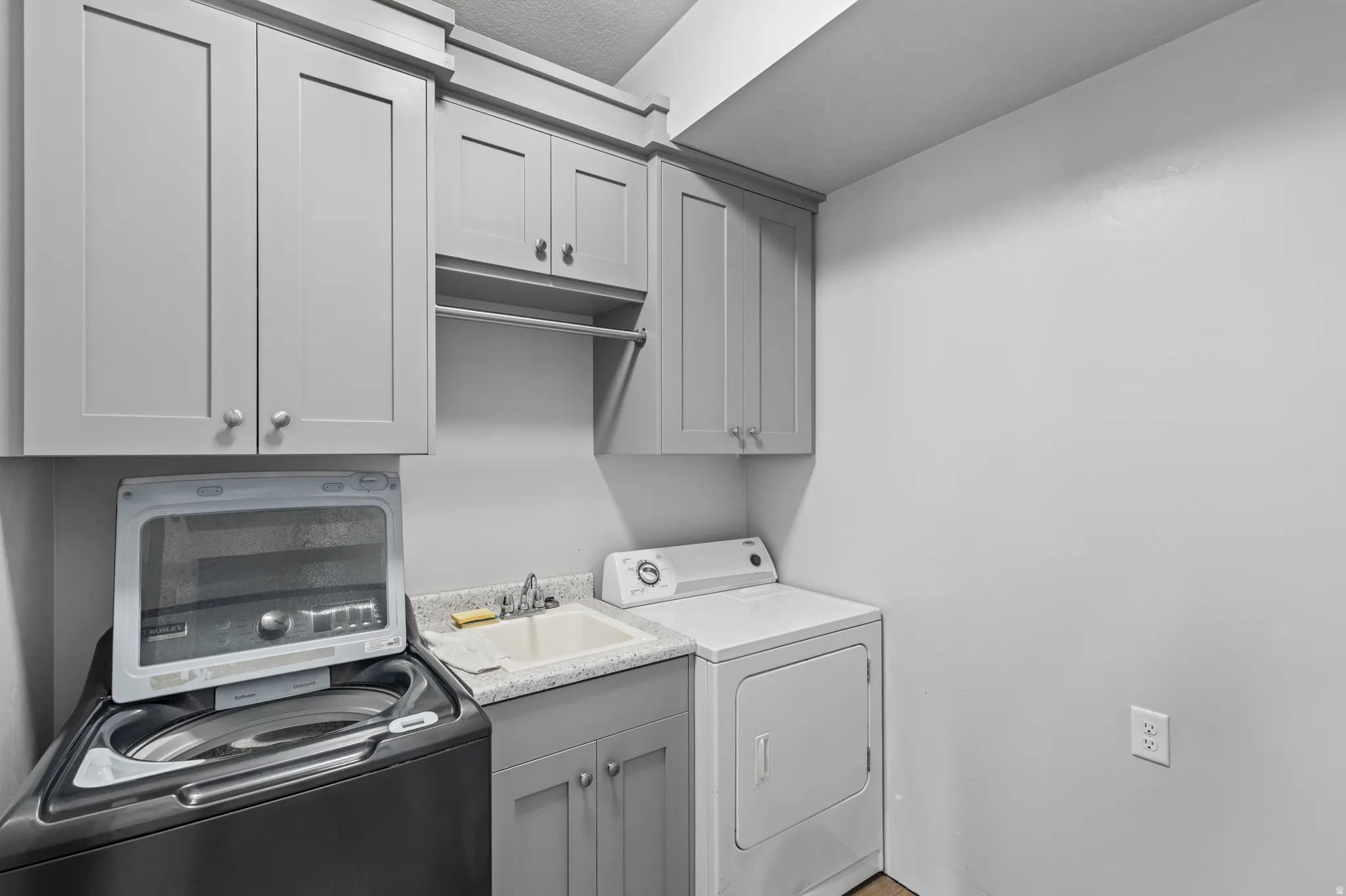 Laundry area featuring built-in cabinetry, a utility sink with a laminate countertop, and a clothes hanging rod