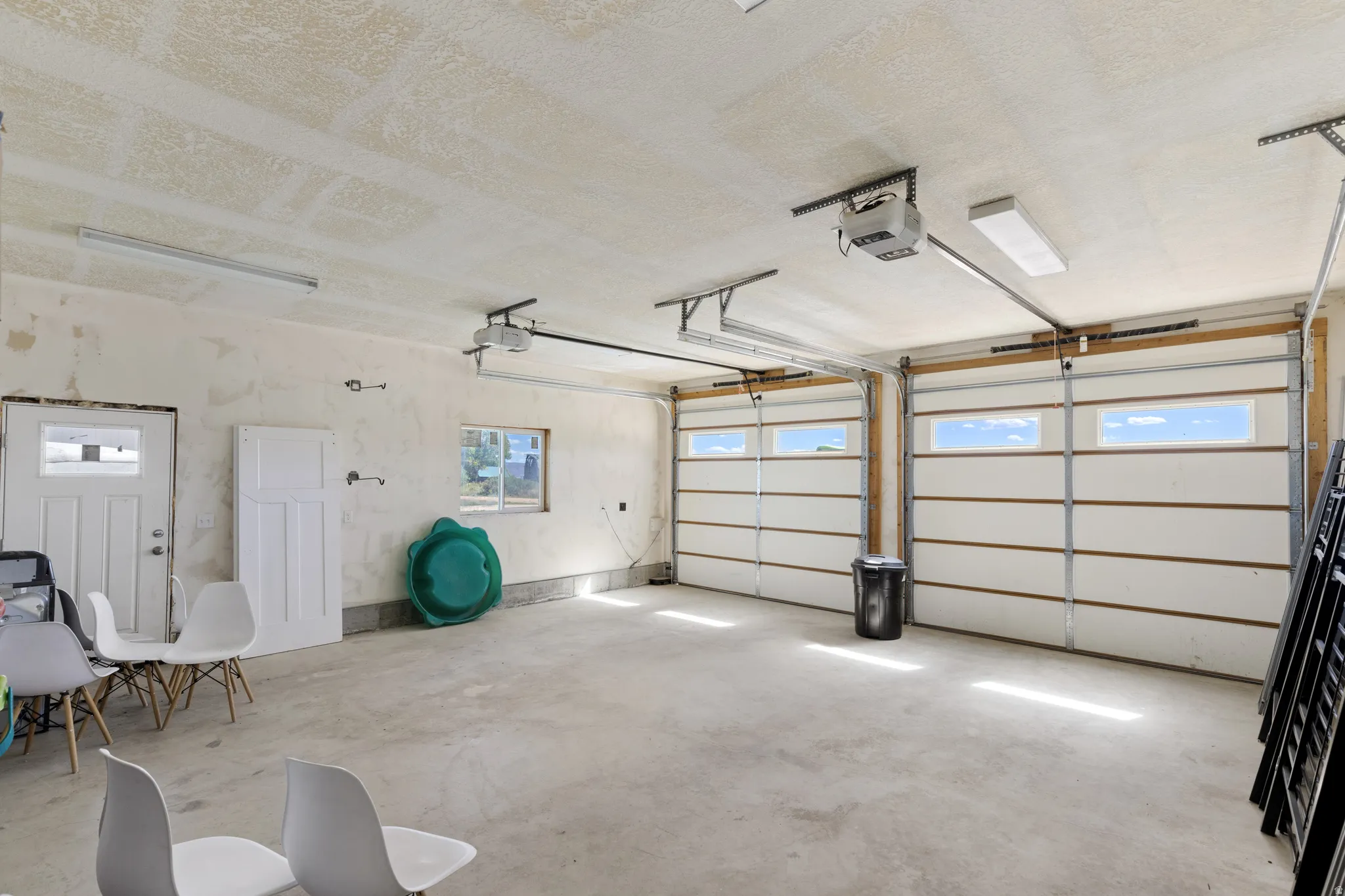 Two garage doors with upper window panels, concrete flooring, overhead lighting, and an additional access door