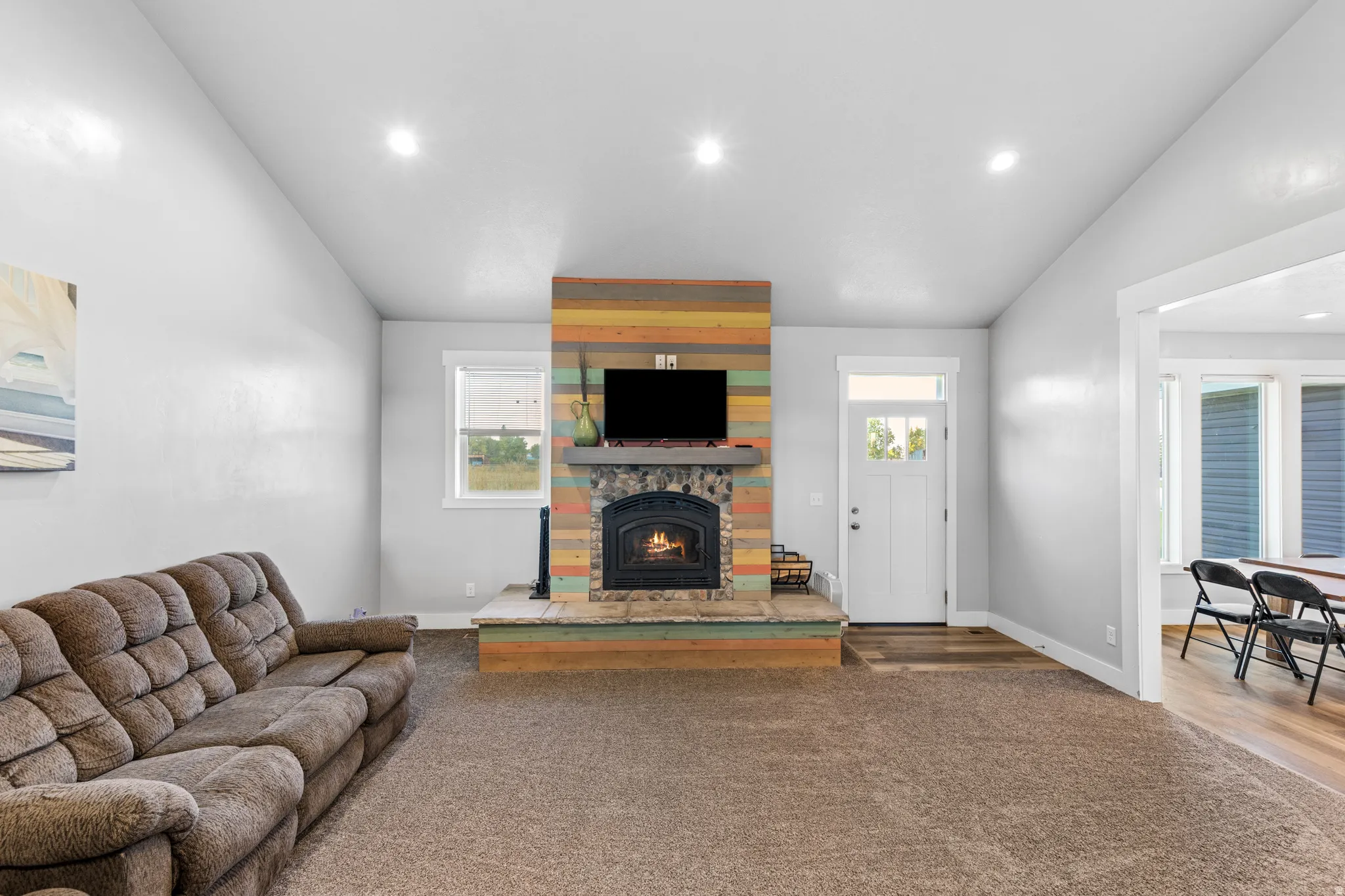 Spacious living area showcasing a wood-burning fireplace with brick surround and wood-finish mantel, recessed ceiling lighting, plush seating arrangement, and direct access to adjacent rooms through multiple doorways
