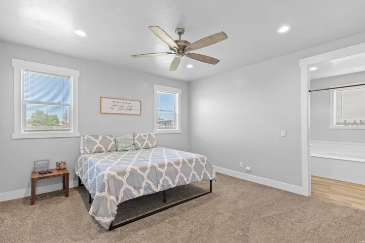 Recessed lighting, ceiling fan, two windows, wall-to-wall carpeting, and an adjacent bathroom with wood-finish flooring and a built-in tub