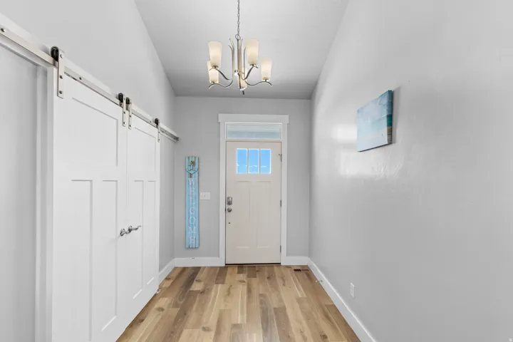 Entryway featuring wood-finish flooring, a contemporary chandelier, a front door with glass panels, and sliding barn doors