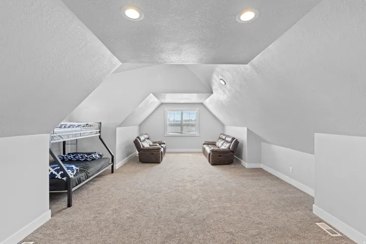 Carpeted flooring in a finished attic space with recessed lighting and a window