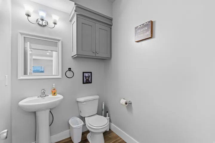 Pedestal sink with chrome faucet, framed wall mirror, overhead vanity lighting, and wall-mounted storage cabinetry