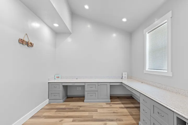 Wood-finish flooring, recessed lighting, built-in gray cabinetry with drawer pulls, integrated countertops, and a window with blinds