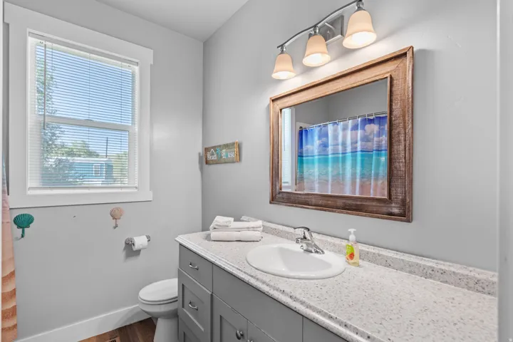 Bathroom featuring a single window, a light gray vanity with a single sink, a light-colored countertop, and a wood-framed mirror
