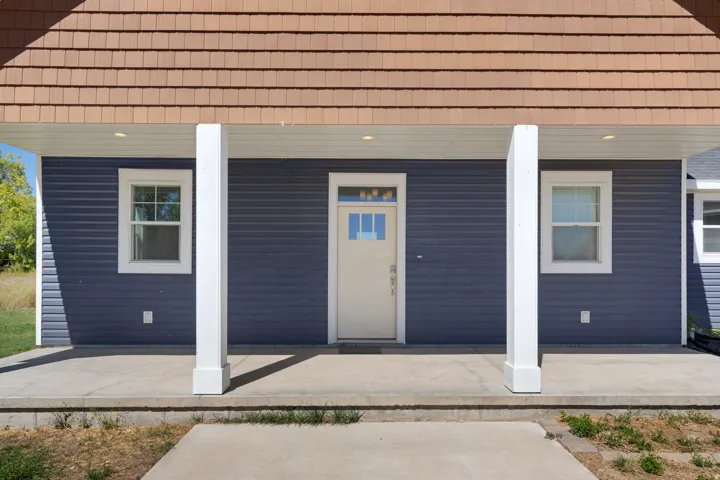 Front entrance with blue horizontal siding, decorative wood-shingle roof, white support columns, recessed ceiling lighting, and a light-colored entry door with glass panels