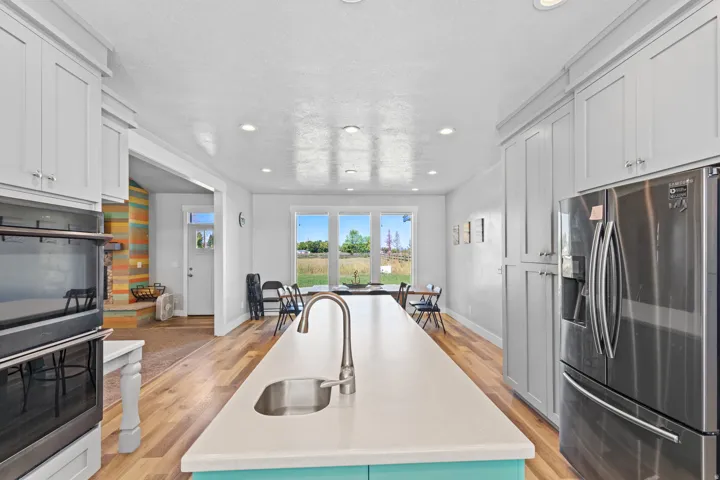 Chef's kitchen featuring white cabinetry, stainless steel appliances including dual refrigerators and built-in wall oven, waterfall-edge quartz island with turquoise base, professional pull-down faucet, recessed ceiling lighting, and hardwood flooring thr