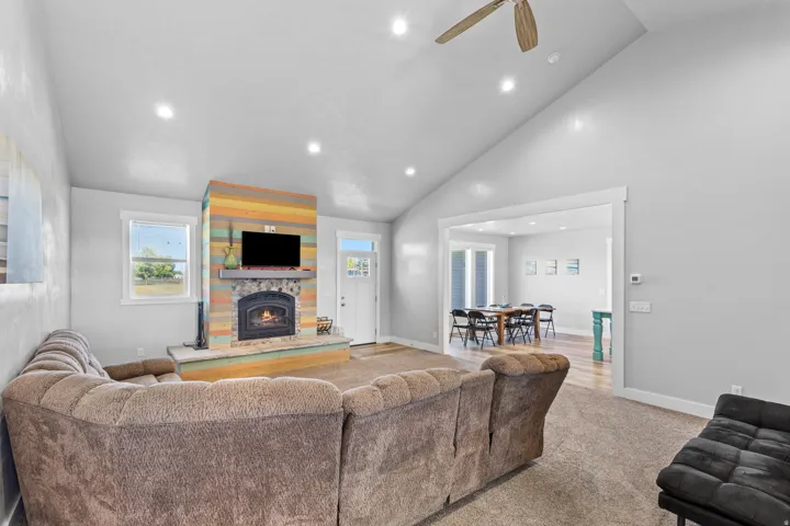 Vaulted ceiling with recessed lighting, stone-clad fireplace, wood-finish flooring, and a ceiling fan