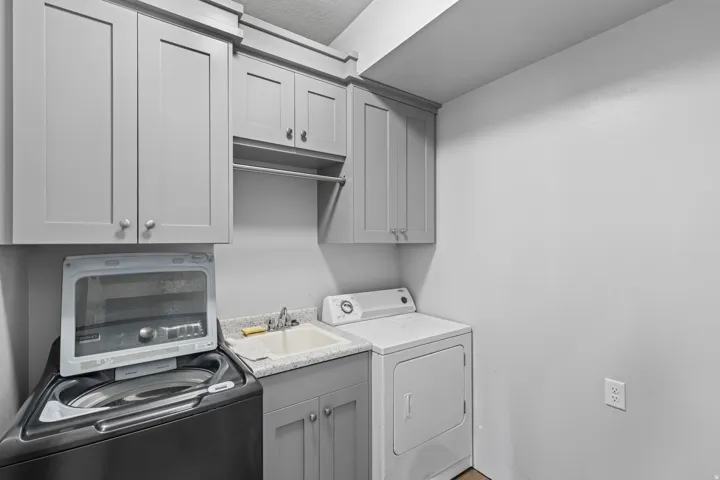 Laundry area featuring built-in cabinetry, a utility sink with a laminate countertop, and a clothes hanging rod