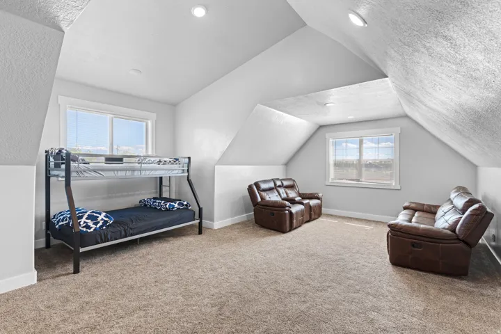 Bright and spacious attic bedroom featuring vaulted ceilings with skylights, abundant natural light from two large windows, neutral carpeting, and ample square footage for multiple functional zones