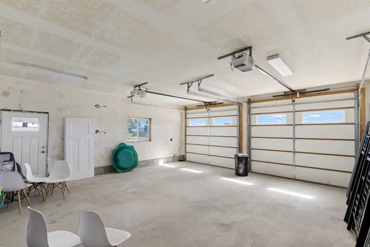 Two garage doors with upper window panels, concrete flooring, overhead lighting, and an additional access door
