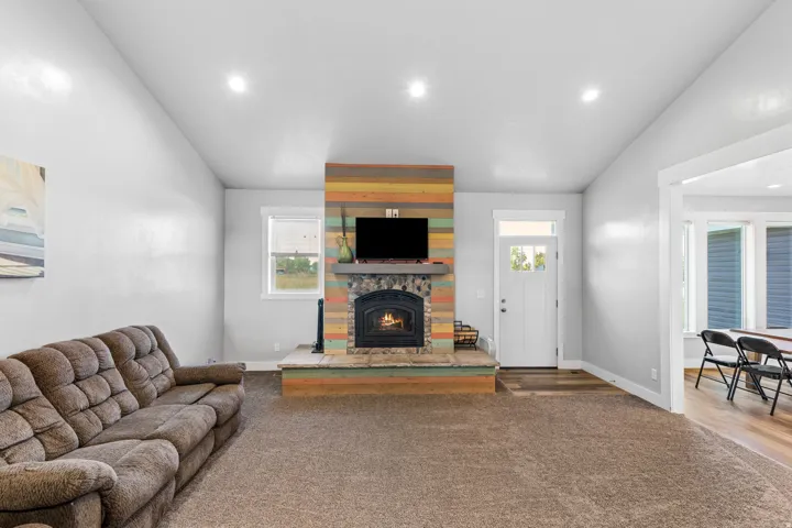 Spacious living area showcasing a wood-burning fireplace with brick surround and wood-finish mantel, recessed ceiling lighting, plush seating arrangement, and direct access to adjacent rooms through multiple doorways